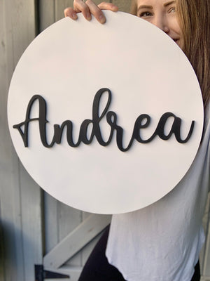 3D round white wooden name sign with black cursive letters spelling Andrea held by woman