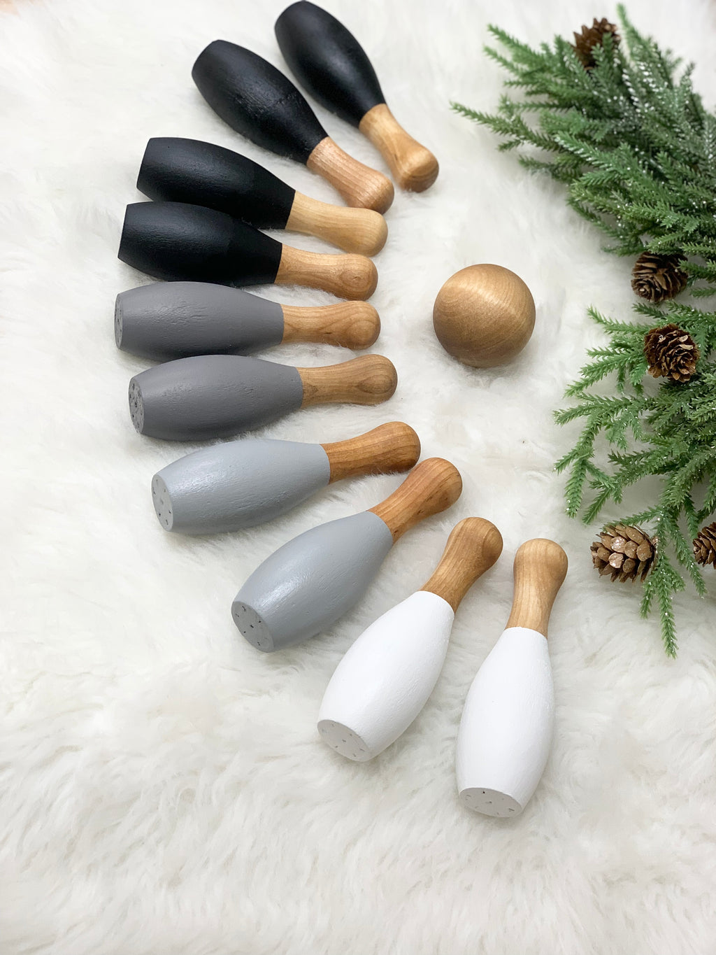 Monochrome wooden bowling set with ten pins in black, gray, and white and one natural wood ball on white fur background