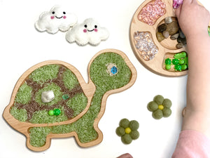 Wooden turtle-shaped sensory tray filled with colored rice and small green beads on white background