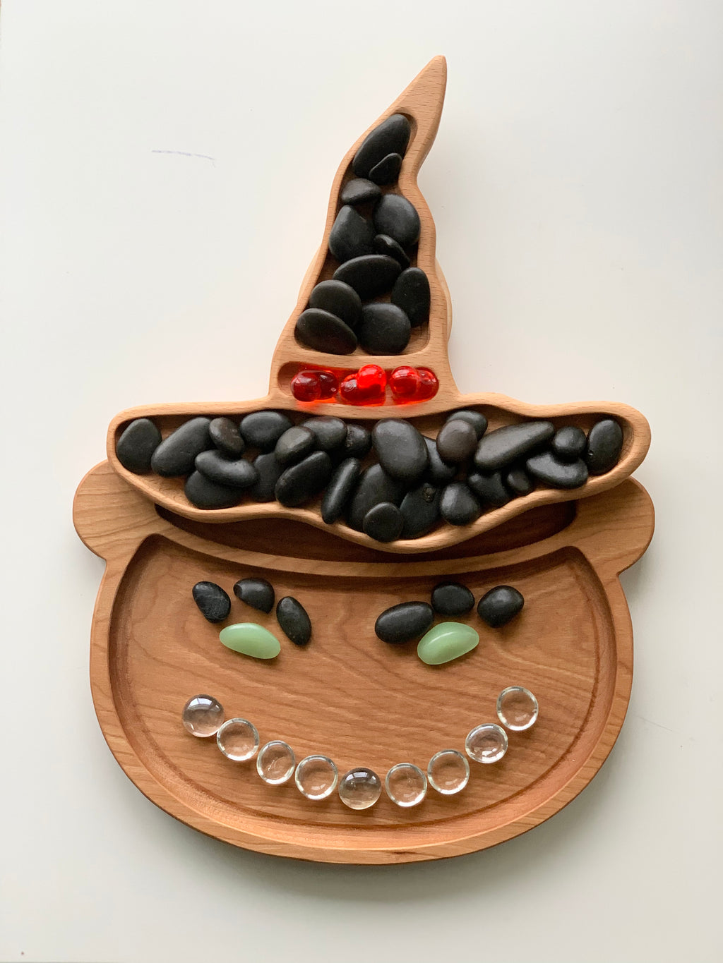 Wooden cauldron-shaped sensory tray with black, red, green, and clear beads arranged like a smiling face