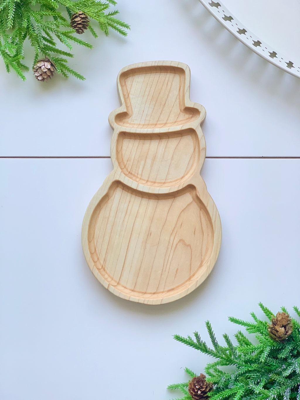 Natural wooden snowman-shaped sensory tray with carved hat, head, and body sections on white surface with pine branches