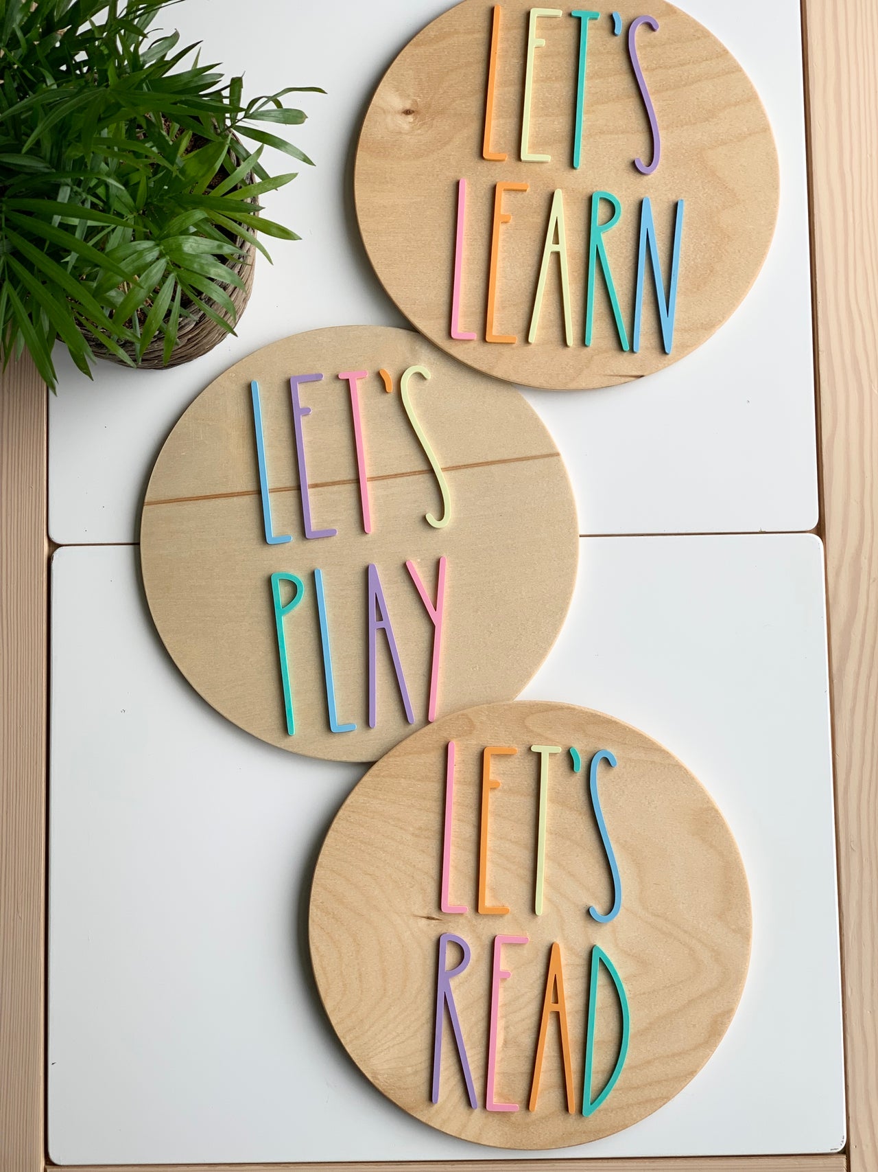 Set of three 10-inch round wooden signs with colorful pastel letters spelling Let's Play, Let's Read, and Let's Learn