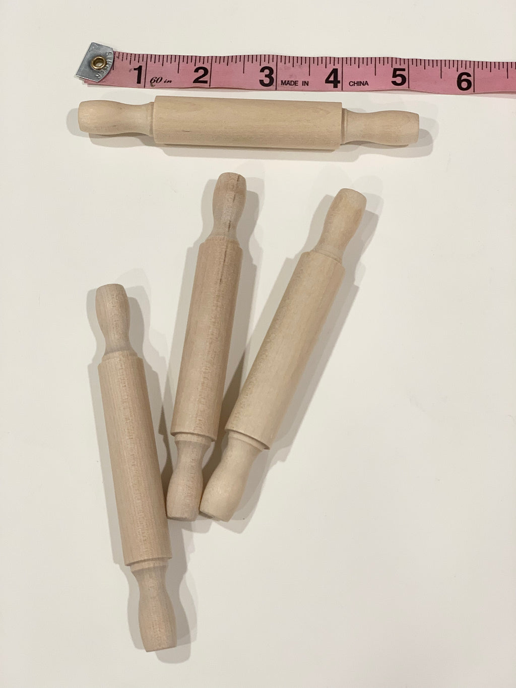 Natural wooden rolling pins for sensory bins with smooth handles and a pink measuring tape on white background