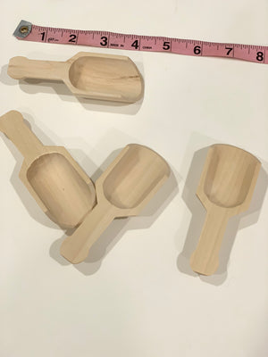 Set of four natural wooden scoops with short handles for sensory bin play on white surface with measuring tape