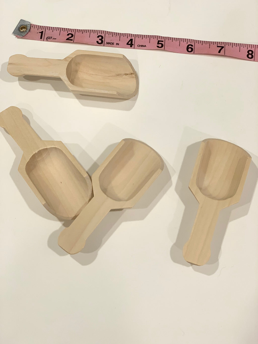 Set of four natural wooden scoops with short handles for sensory bin play on white surface with measuring tape