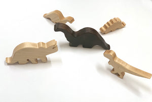 Set of five small wooden dinosaur toy figurines in various natural wood tones on white background