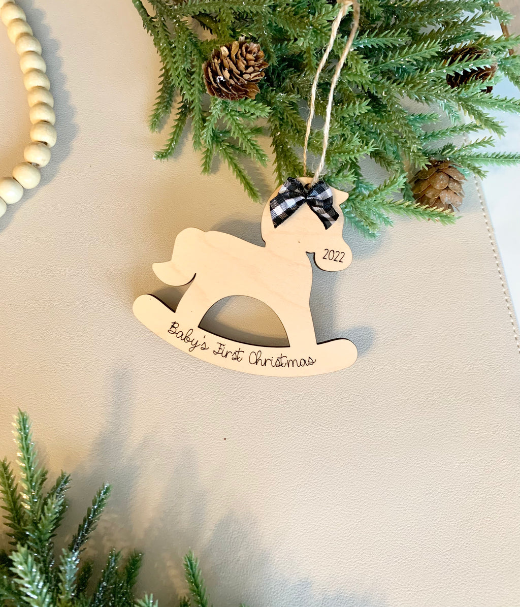 Wooden rocking horse baby’s first Christmas ornament with black gingham bow and engraved year 2022 hanging on greenery