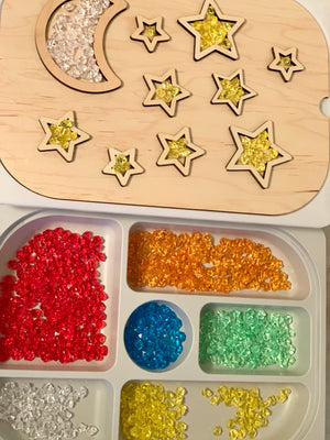 Maple wood night sky insert with moon and star shapes filled with yellow and clear translucent beads on white tray with colorful gems