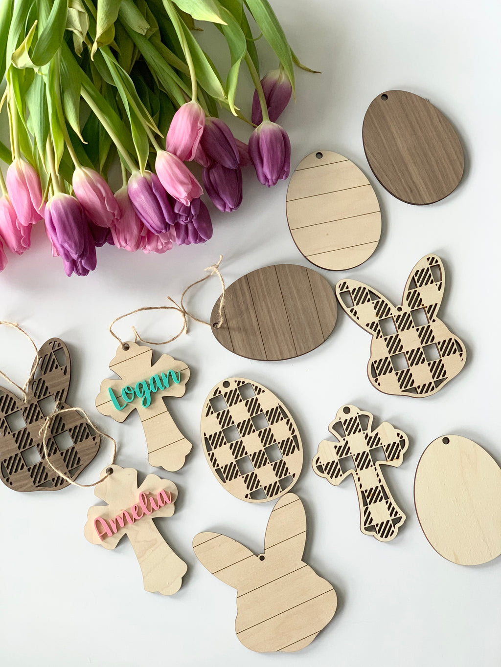 Assorted wooden Easter basket name tags in egg, bunny, and cross shapes with plaid and striped designs on white background