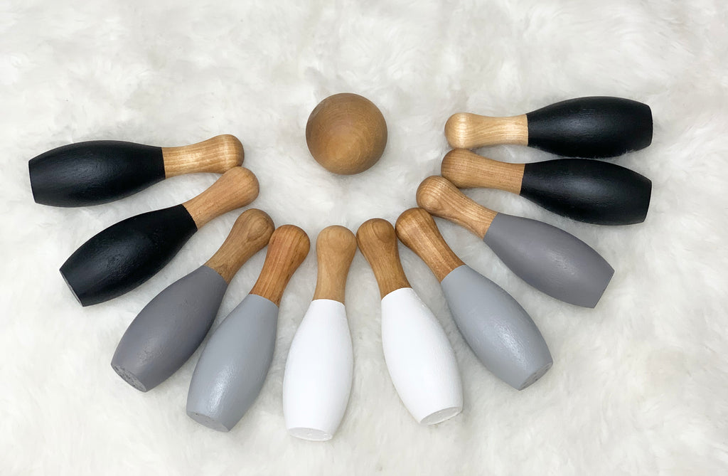 Monochrome wooden 10-piece toddler bowling set with natural wood ball and painted black, gray, and white pins on white background