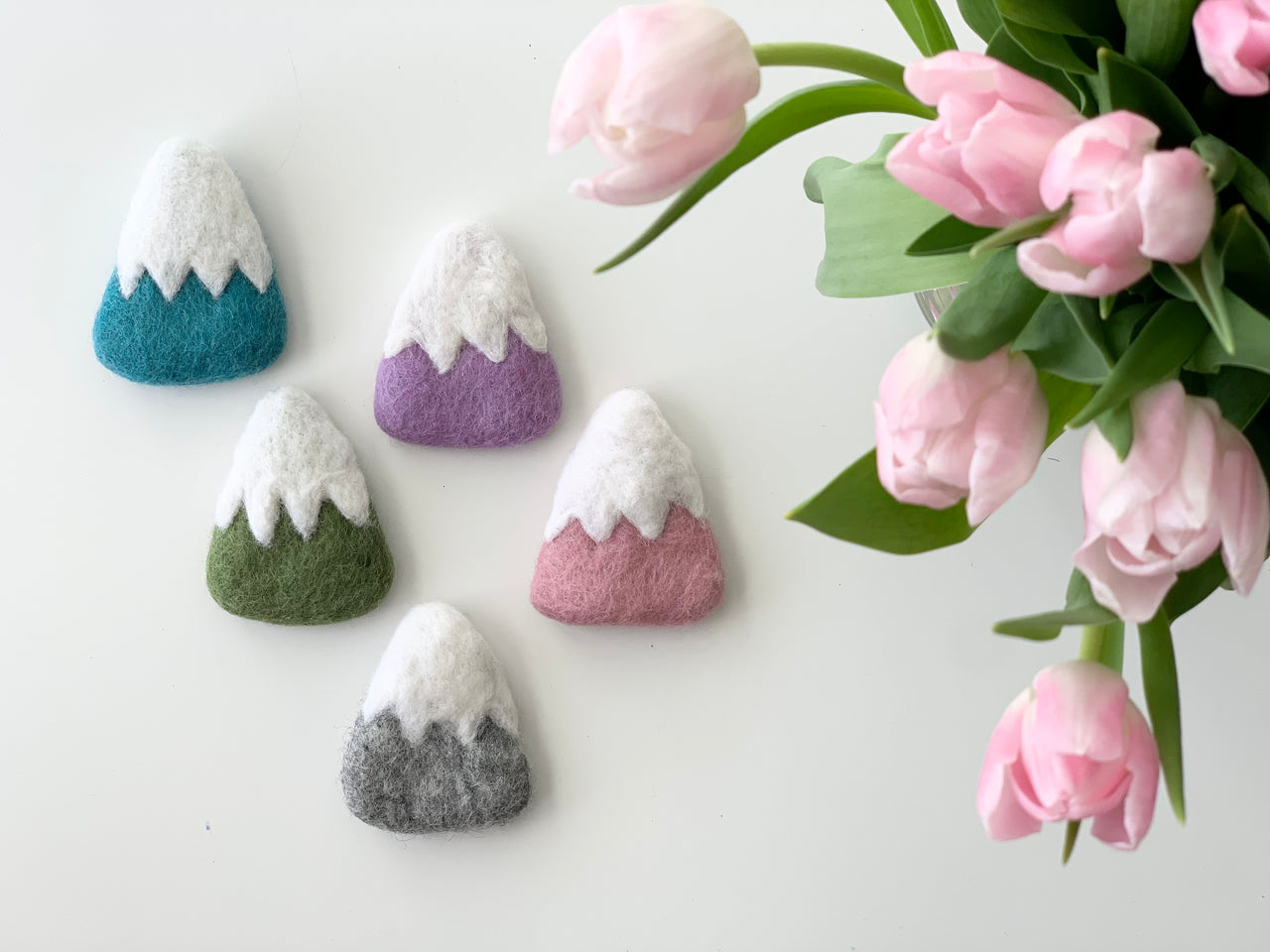 Set of five handmade felt mountain ornaments in various colors with pink tulips on white background