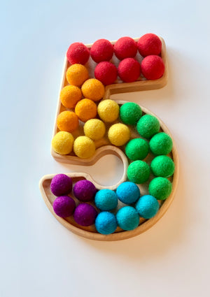 Wooden sensory tray shaped as number 5 filled with colorful felt balls in rainbow colors on white background