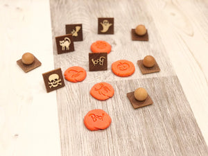 Small wooden Halloween play dough stamps with pumpkin, ghost, cat, and skull designs on light wood surface