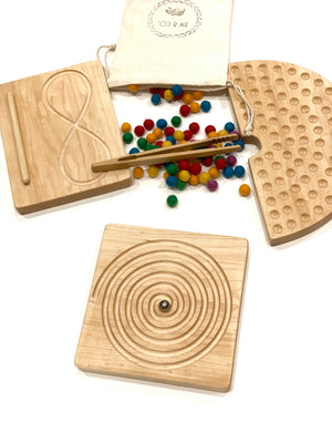 Natural maple wooden tracing boards with engraved paths, colorful pom-poms, tweezers, and a cotton drawstring bag on white background