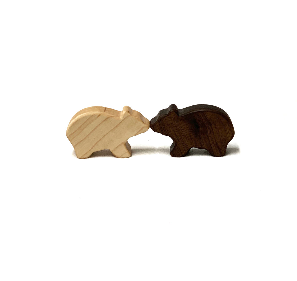 Two small handcrafted wooden bear figurines, one light and one dark, on white background