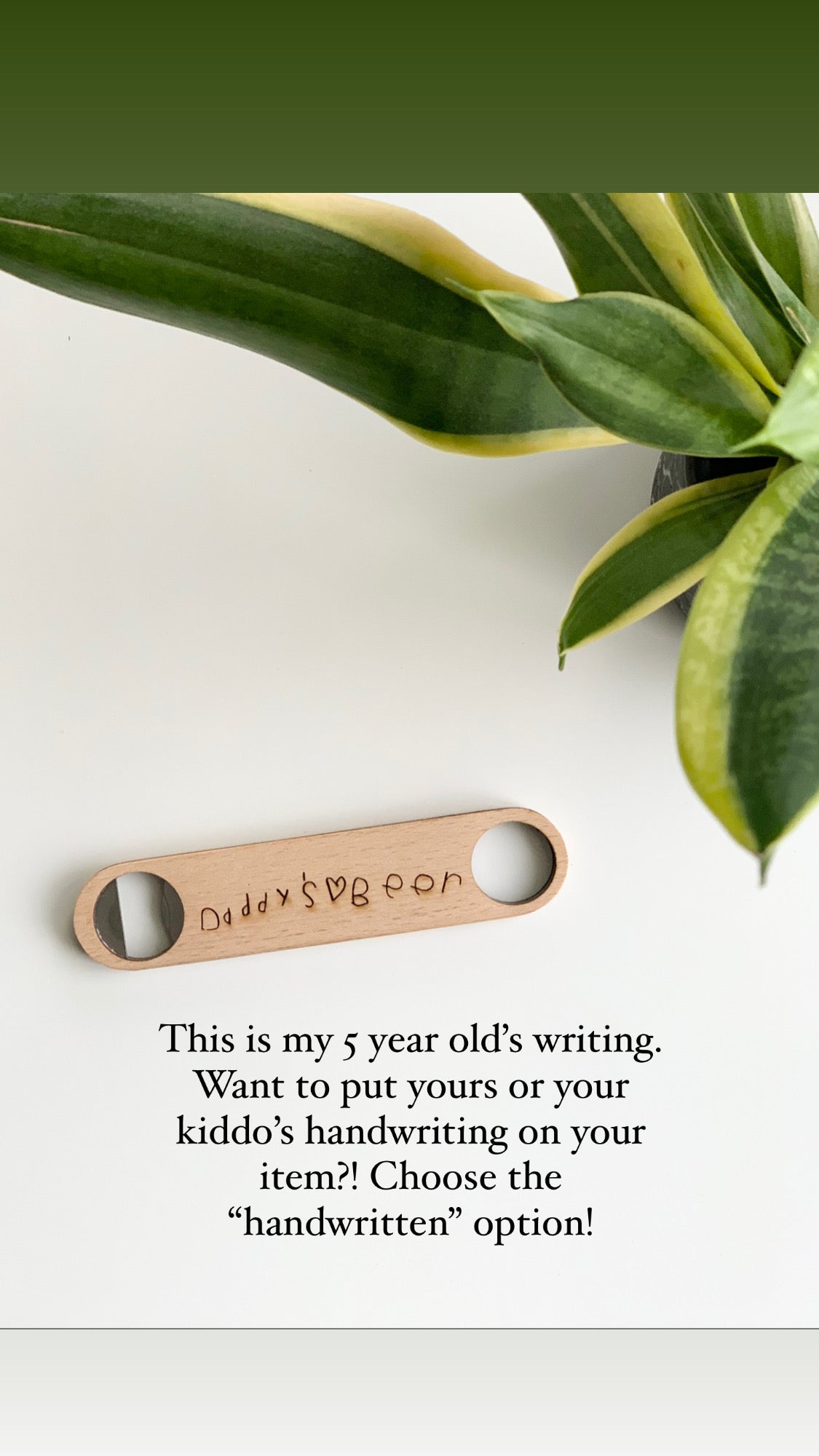 Custom wooden barbecue scraper engraved with child's handwriting on light wood surface near green plant leaves