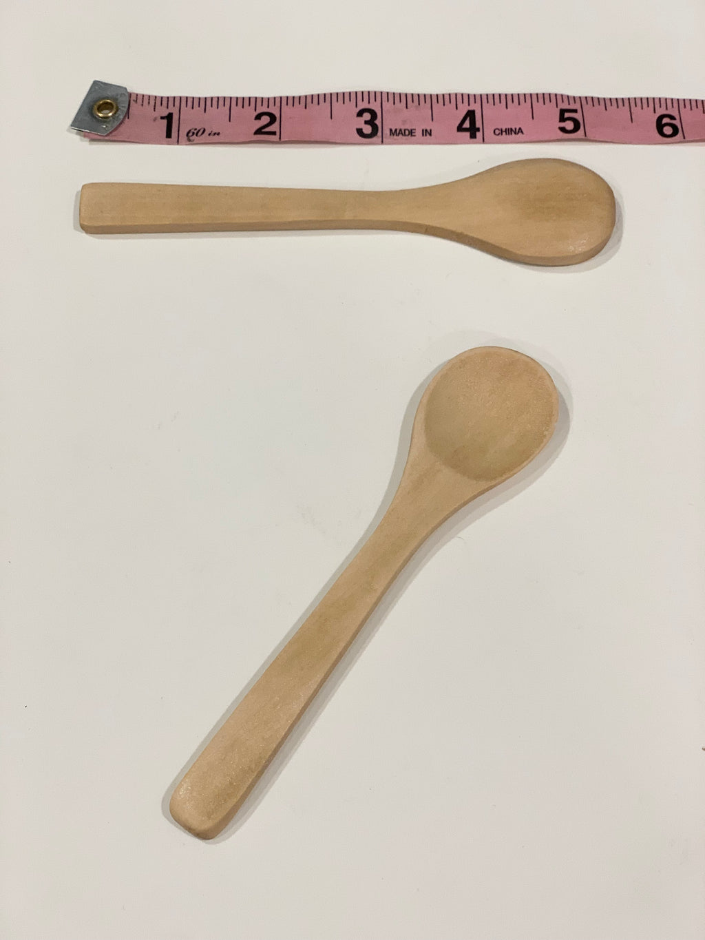 Two small natural wooden sensory bin spoons with rounded handles next to a pink measuring tape on white surface