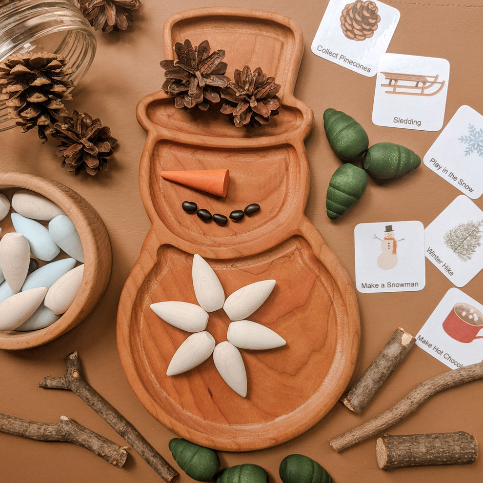 Wooden snowman sensory tray with pinecones, wooden seeds, and nature-themed activity cards on tan background