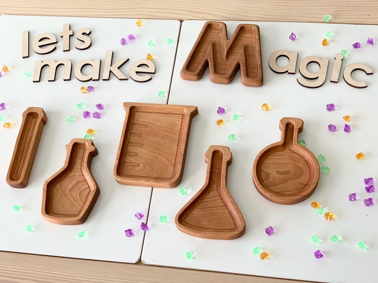 Set of wooden potion bottle plates and science beaker sensory trays on white background with scattered colorful crystals
