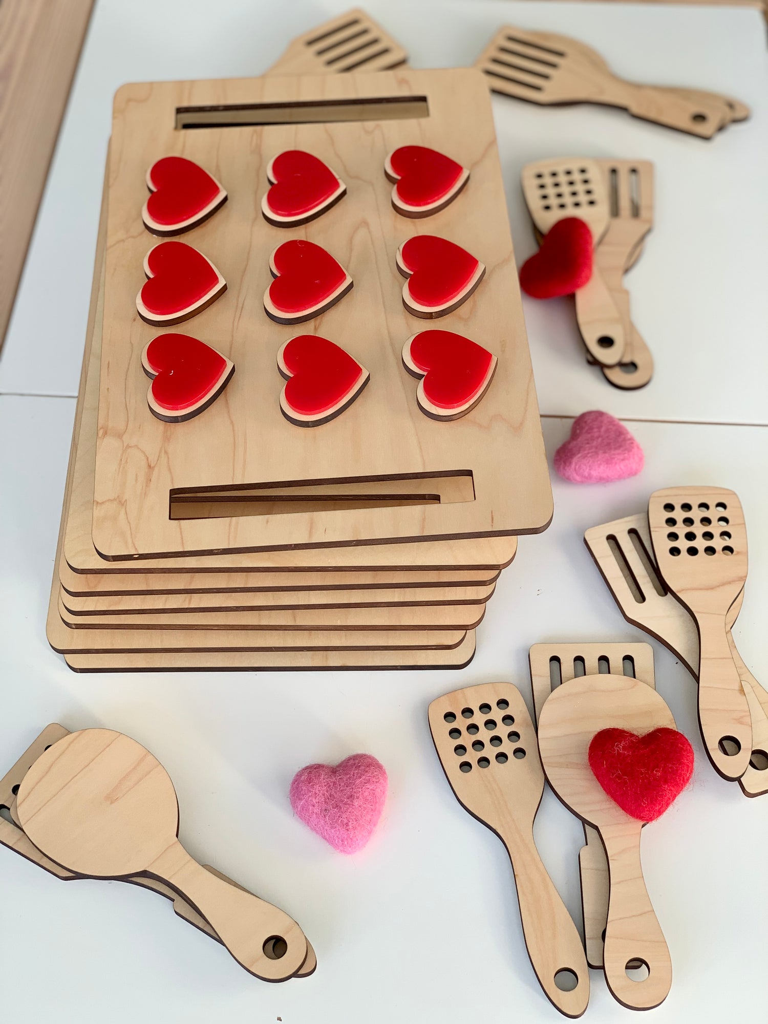 Stack of wooden cookie sheets with red heart-shaped cookies and wooden spatulas scattered on white surface