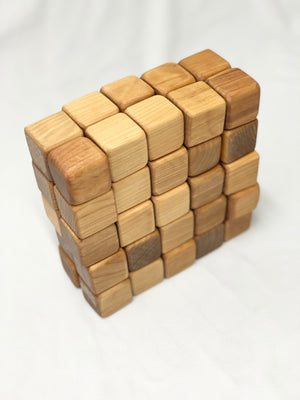 Natural unfinished 2-inch wooden blocks stacked in a grid pattern showing varied wood tones on white fabric background