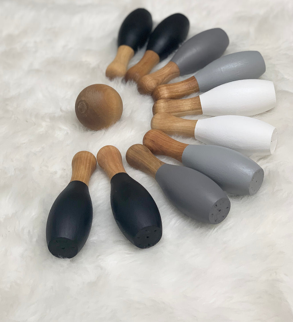 Monochrome 10-piece wooden bowling set with natural wood ball and black, gray, and white pins on soft fabric background