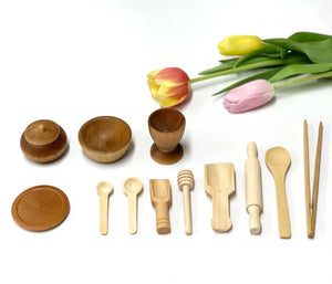 Small wooden sensory bin tools including bowls, spoons, rolling pin, honey dipper, and chopsticks on white background with tulips