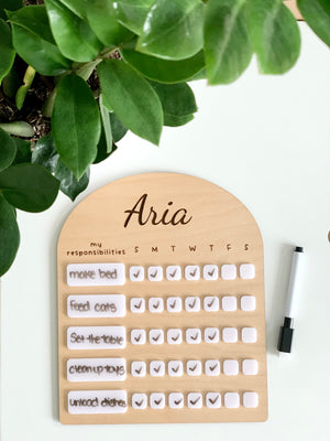 Personalized wooden chore chart with white acrylic dry erase tiles and black dry erase marker on white surface