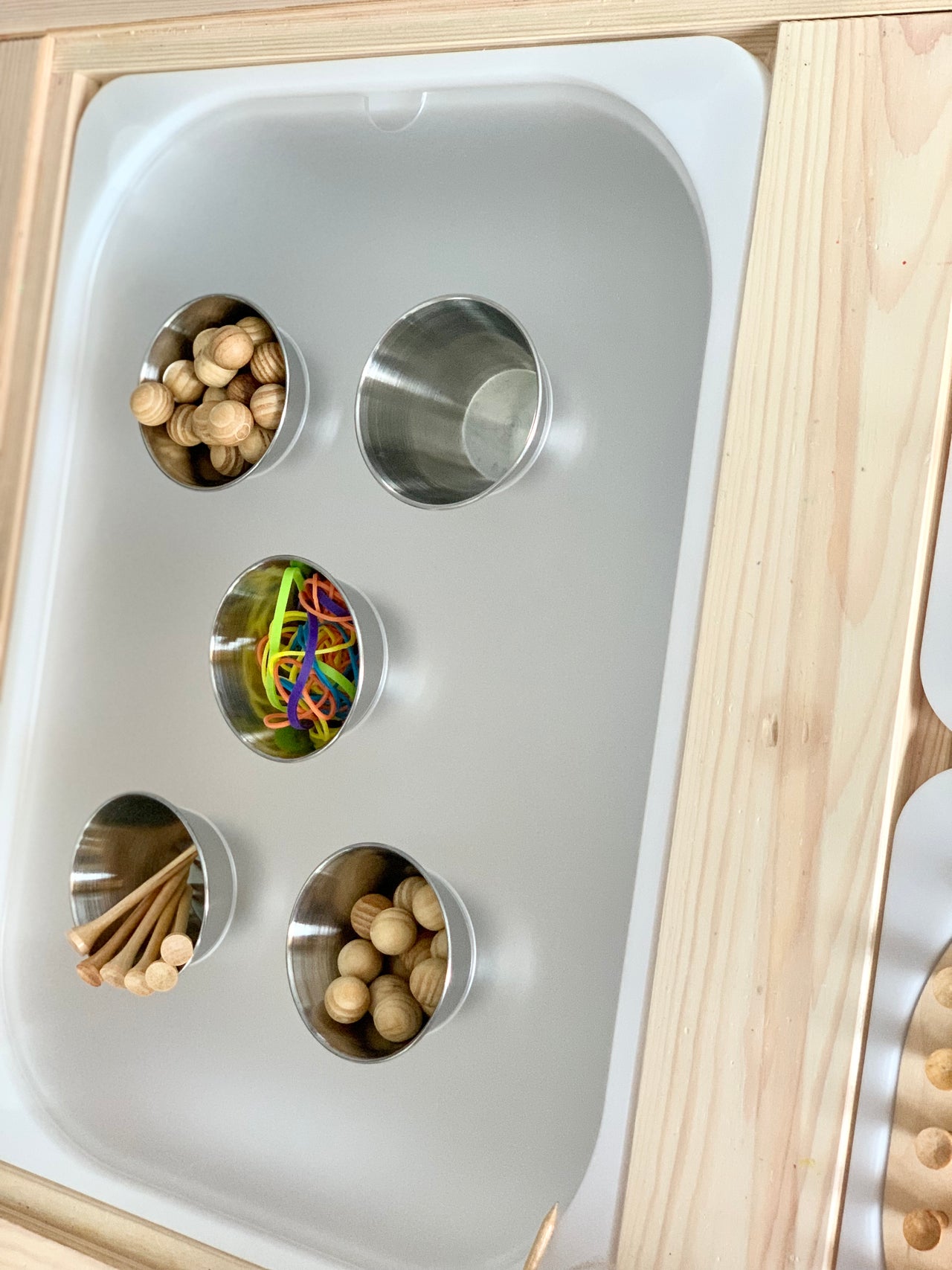Trofast Flisat maple plywood tabletop insert with five metal cups holding wooden balls, sticks, and colorful bands on gray base