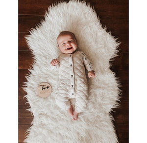 Smiling baby lying on white fluffy rug next to wooden disc engraved with two months milestone text