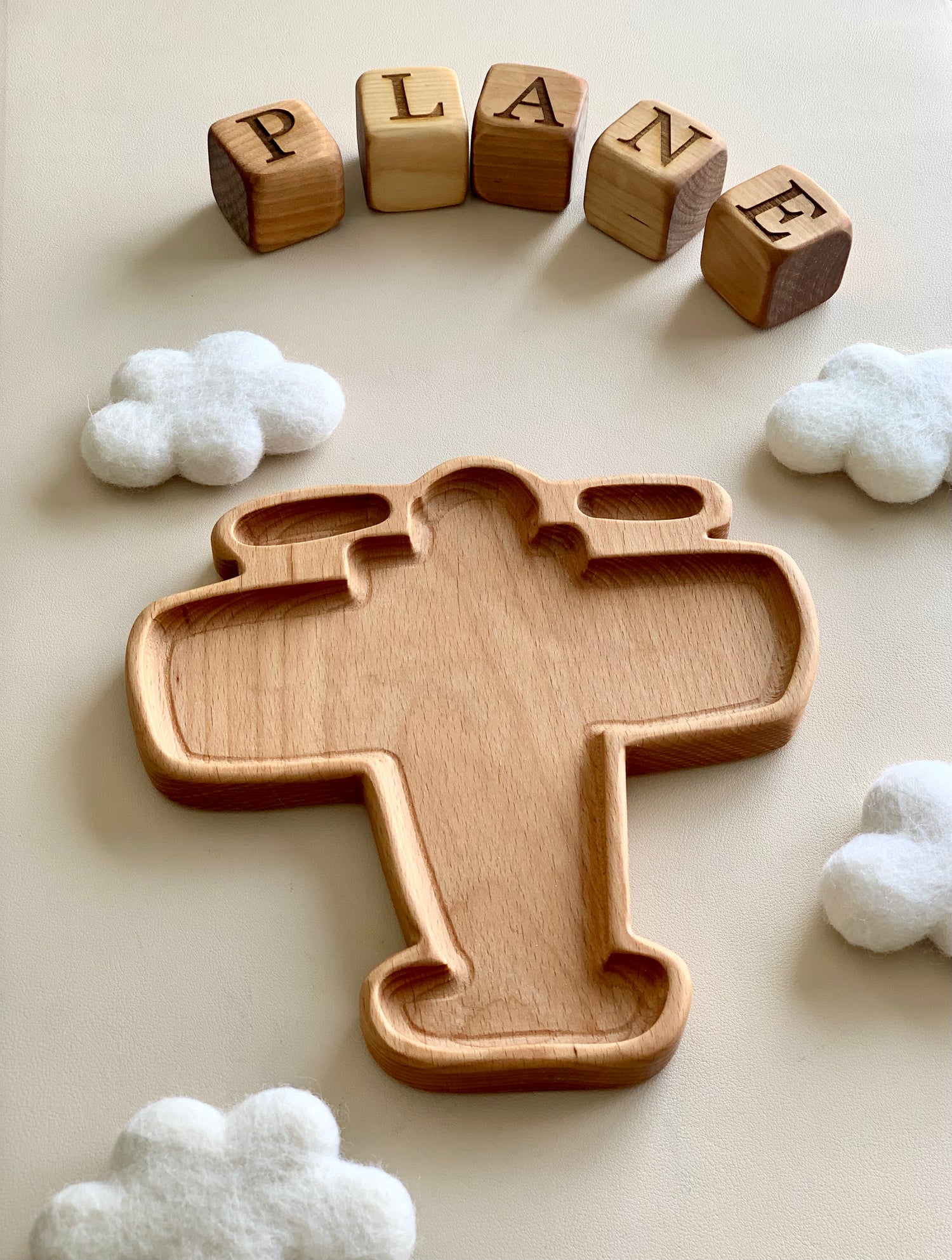 Wooden airplane-shaped sensory tray surrounded by felt clouds and wooden blocks spelling plane on neutral surface