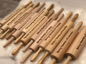 Assorted personalized wooden rolling pins with custom wood burned messages on smooth wood surface arranged on soft fabric