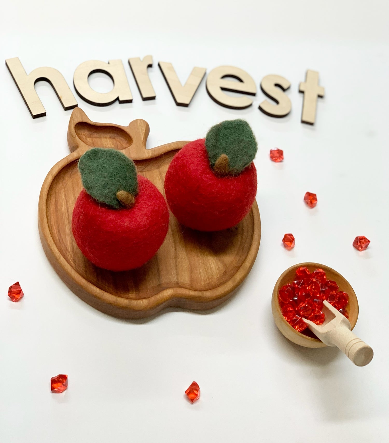 Small wooden apple-shaped plate with two red felt apples and red gem decorations on white background