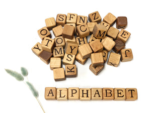 Natural 2-inch wooden alphabet blocks with engraved capital letters scattered and arranged to spell ALPHABET on white background