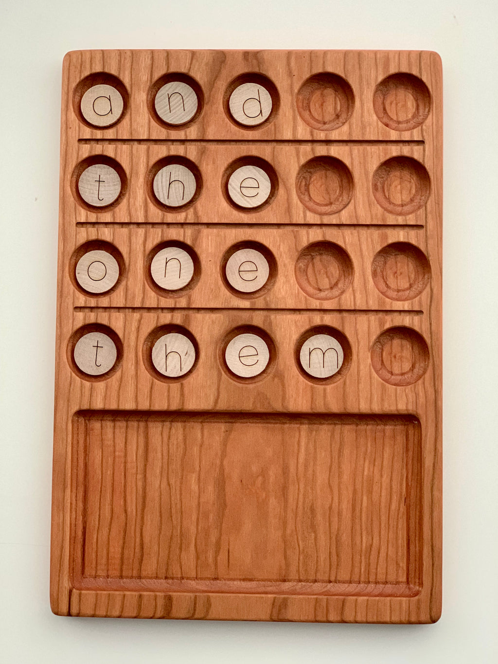 Set of small round wooden alphabet discs with simple laser-engraved lowercase letters in carved wooden tray slots