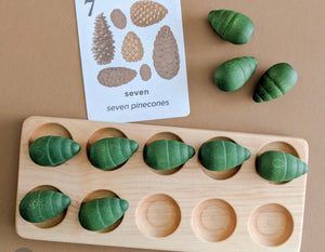 Natural wooden ten frame tray with eight green wooden pinecone counters and a counting card showing seven pinecones