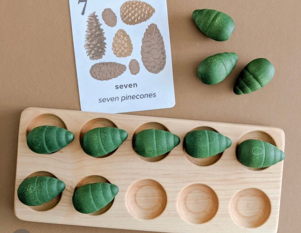 Natural wooden ten frame tray with eight green wooden pinecone counters and a counting card showing seven pinecones