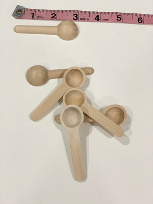 Natural wooden sensory bin scoops arranged with a pink measuring tape on white background