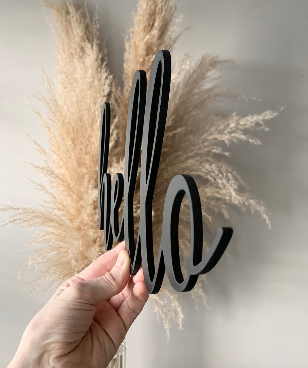 Hand holding custom black cursive word cutout sign with dried pampas grass background on neutral wall