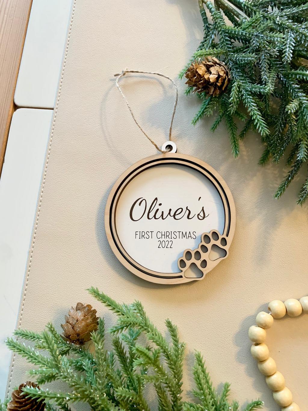Round wooden pet-themed Christmas ornament with paw prints and personalized name for first Christmas 2022
