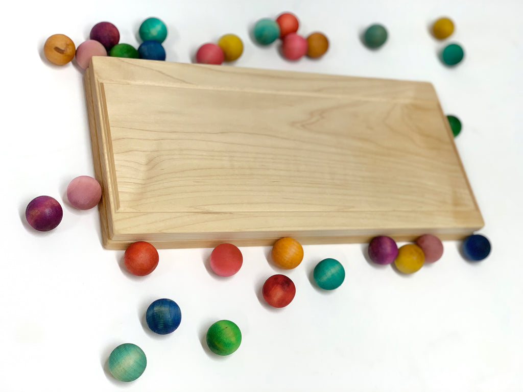 Smooth natural wooden rectangular board surrounded by scattered colorful round wooden beads on white background