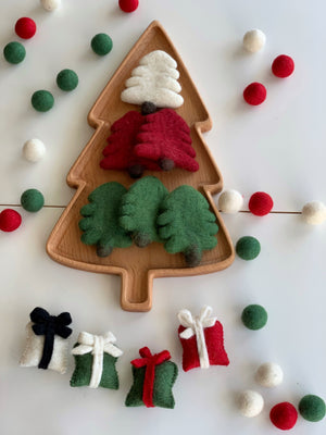 Large wooden tree-shaped plate holding red, green, and white felt pine trees surrounded by felt balls and gift shapes on white surface