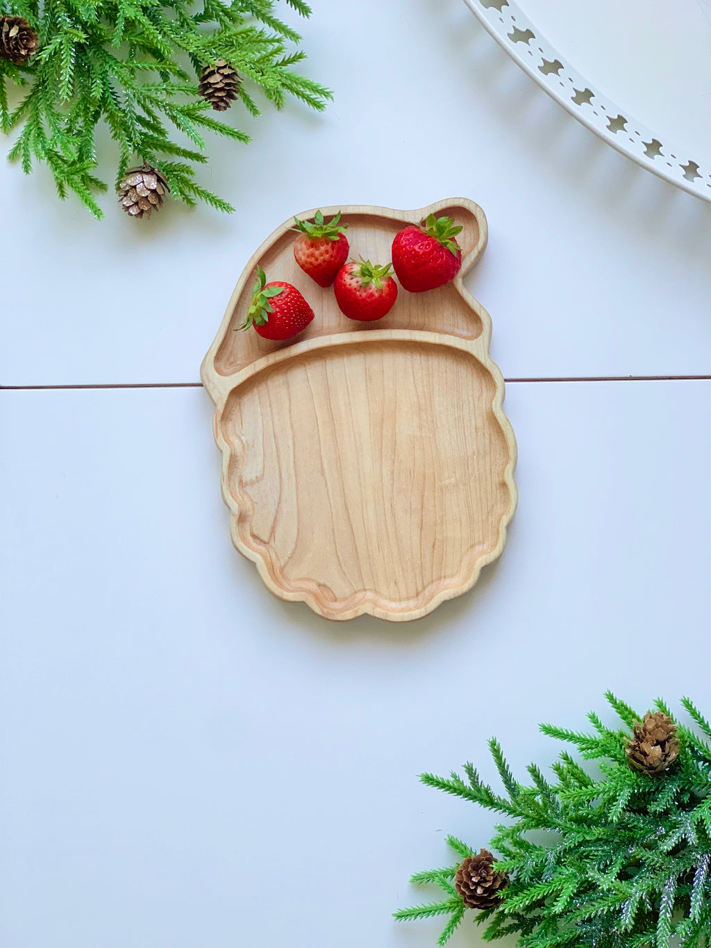 Natural wooden Santa face-shaped sensory tray with strawberries in hat section on white background with pine branches