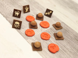 Set of small wooden Halloween play dough stamps with carved ghost, cat, bat, skull, and pumpkin designs on light wood surface
