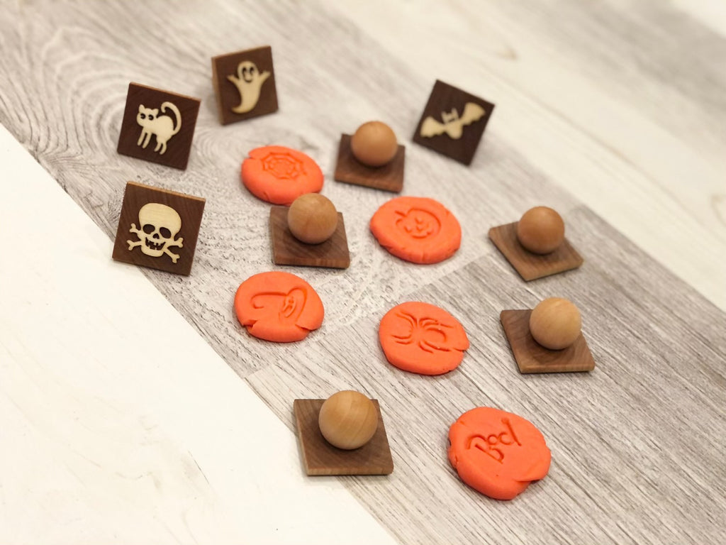 Set of small wooden Halloween play dough stamps with carved ghost, cat, bat, skull, and pumpkin designs on light wood surface