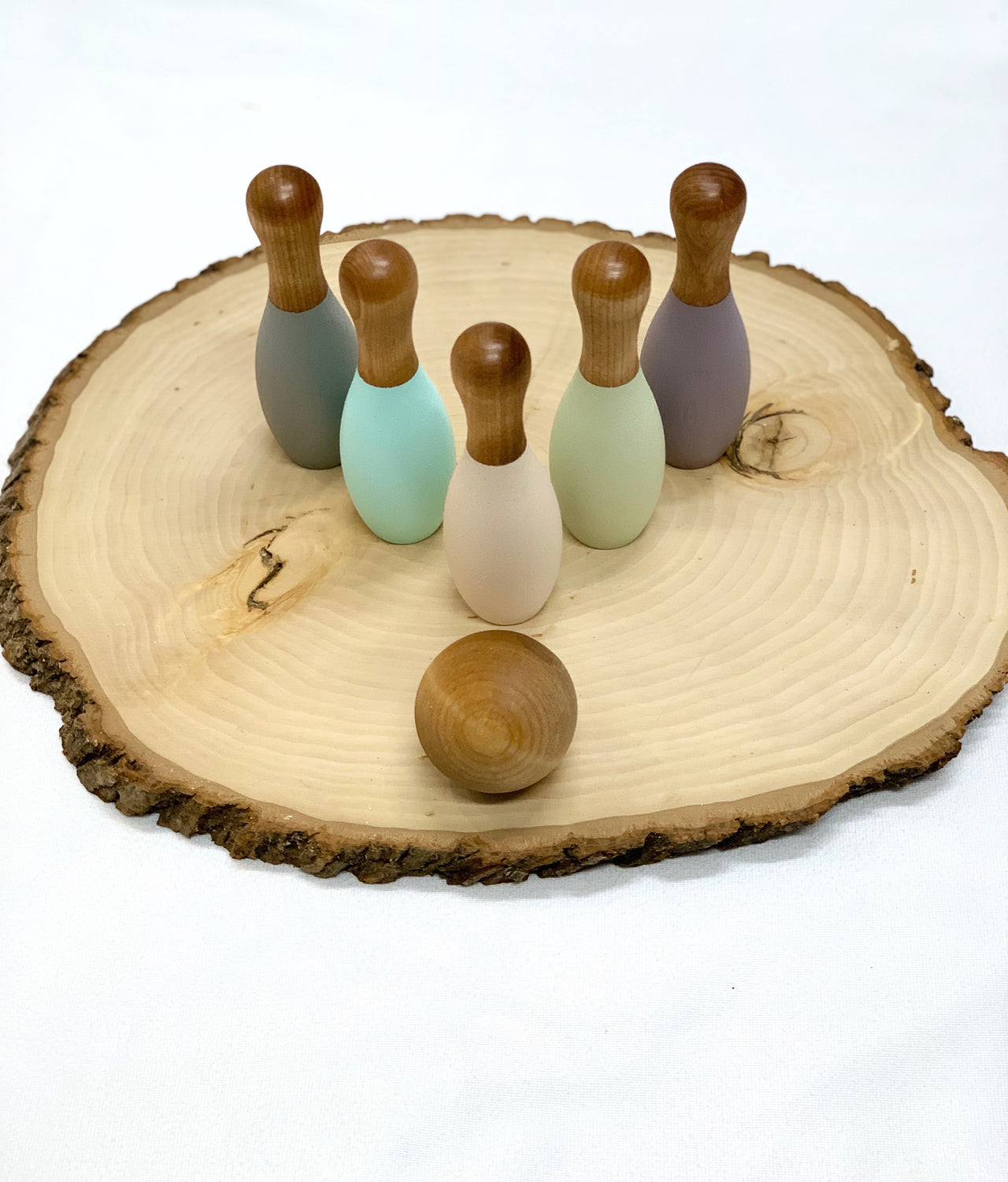 Wooden pastel bowling set with five pins and one ball displayed on a natural wood slice surface