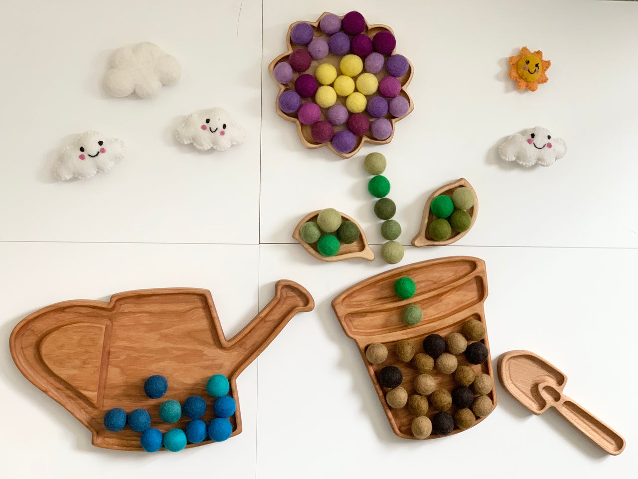 Wooden garden spade sensory tray with colorful felt balls and watering can tray with blue felt balls on white background