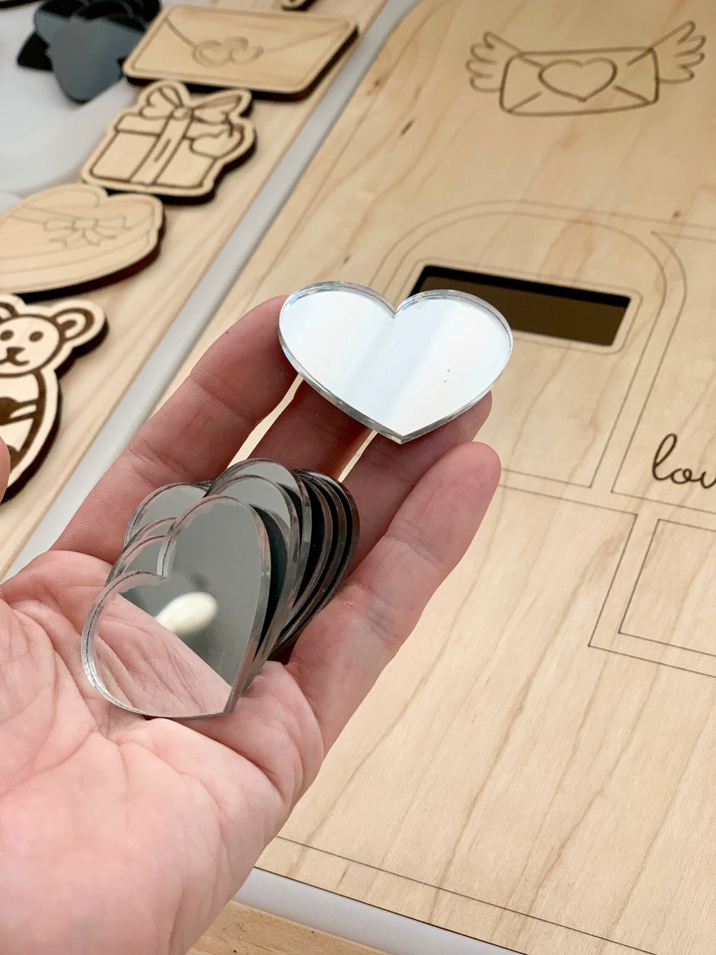 Hand holding set of 7 clear laser-cut heart acrylic shapes for sensory loose parts play on wooden surface