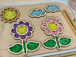 Wooden tray puzzle filled with colorful mini acrylic treasure gems in shapes of flowers, leaves, sun, and clouds on table