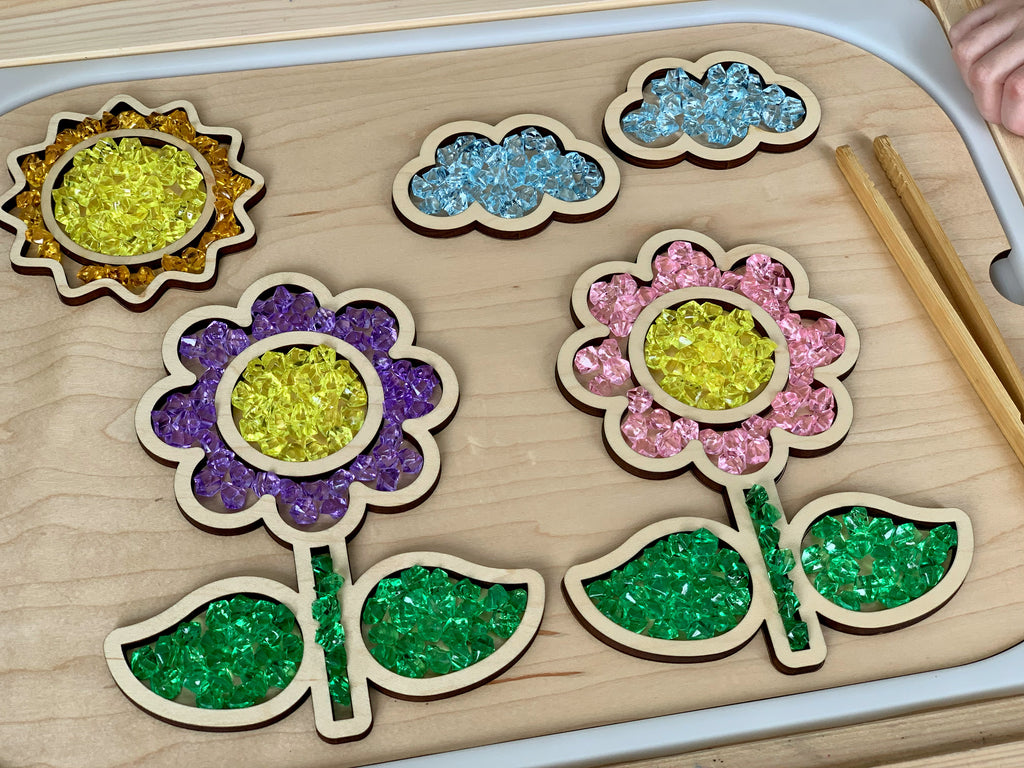 Wooden tray puzzle filled with colorful mini acrylic treasure gems in shapes of flowers, leaves, sun, and clouds on table